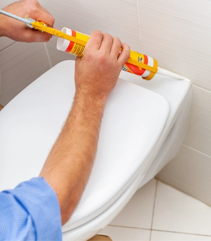 professional bathroom caulking in falls church va showing a technician applying a fresh bead of silicone sealant around a white toilet base.