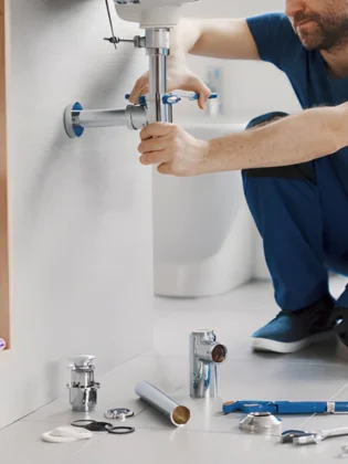 professional technician performing a bathroom sink repair, specifically focusing on the installation and tightening of a chrome p-trap assembly beneath a white vanity.