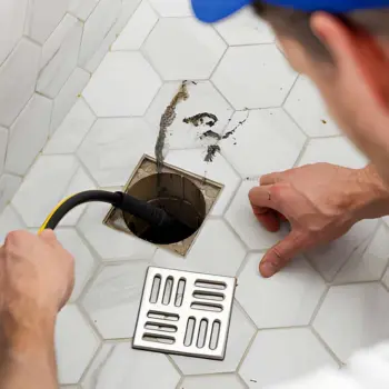 a professional drain cleaning service in progress, showing a technician using a specialized high-pressure water jetting tool to clear deep-seated debris from a square tile-integrated shower drain.