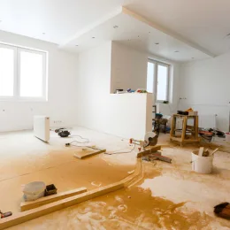 interior view of a residential renovation project managed by expert home remodeling contractors, showing a room with fresh white walls, natural light from large windows, and active construction staging with tools and building materials.