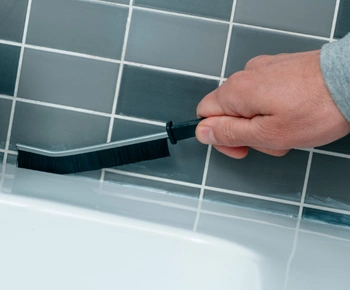 hand using a grout cleaning brush to restore grout lines between bathroom tiles during grout restoration service.