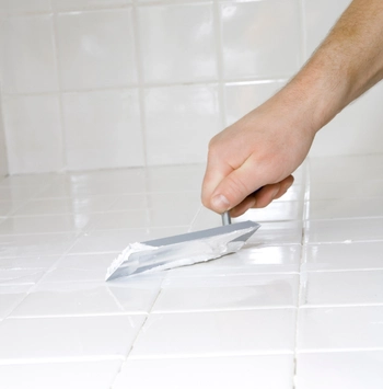 hand applying fresh grout between white ceramic tiles during professional tile grouting service.