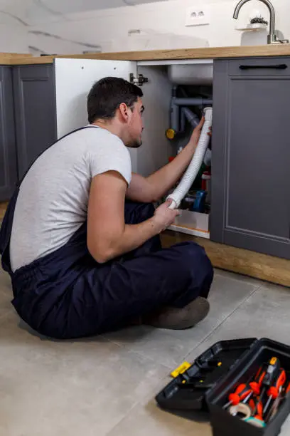 kitchen sink leak repair in falls church va with plumber fixing drain pipe under kitchen cabinet