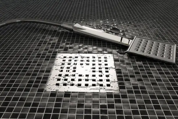 shower floor drain with removable grate next to handheld shower head during shower drain repair service.