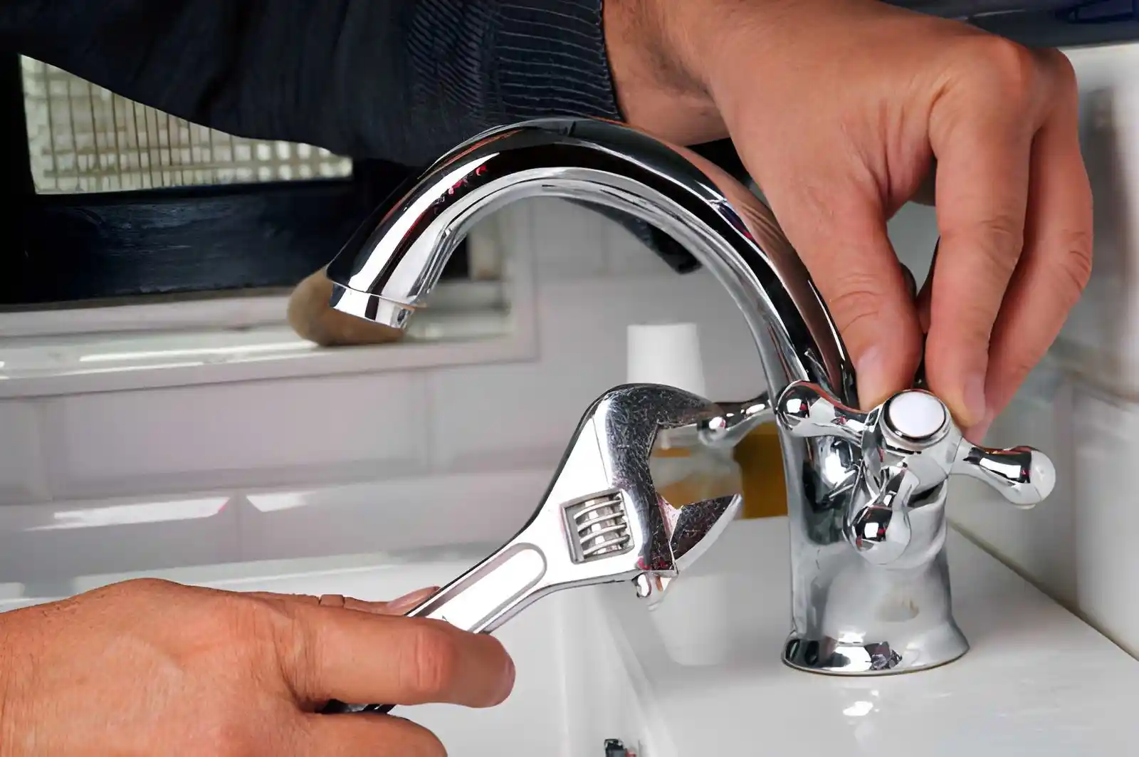 plumber tightening a bathroom sink faucet with a wrench during sink repair service, sink repair and installation in merrifield va