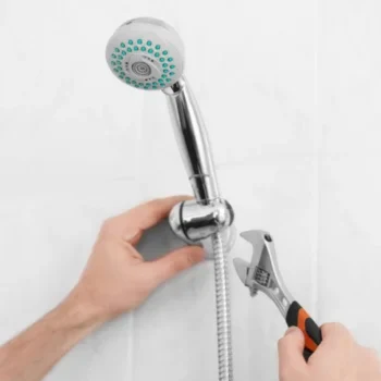 professional shower faucet repair in arlington, va, featuring a technician’s hands using a crescent wrench to secure a chrome handheld showerhead bracket against a white tiled wall.
