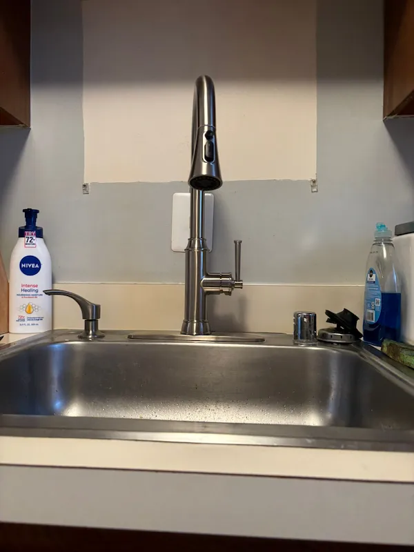 A newly installed high-arc brushed nickel pull-out kitchen faucet on a stainless steel sink, completed as part of a home plumbing upgrade in Burke, VA.
