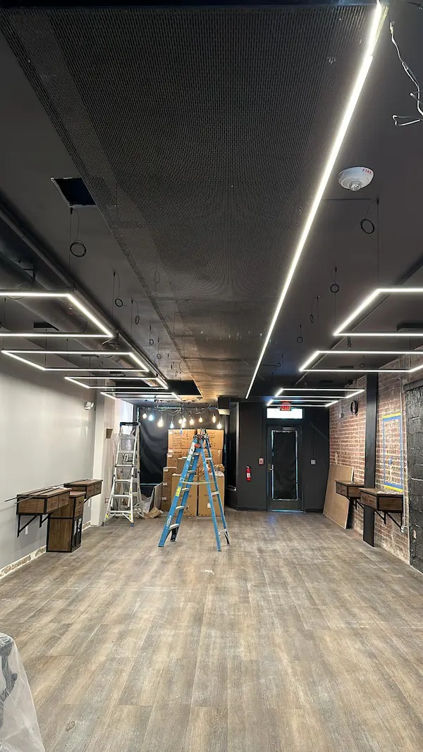 Completed commercial electrical remodel in Falls Church, VA, highlighting architectural square LED pendant light fixtures hanging from a black industrial ceiling, custom wood flooring, and brick accent walls.